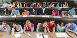 Bored college students asleep on desks in lecture hall classroom